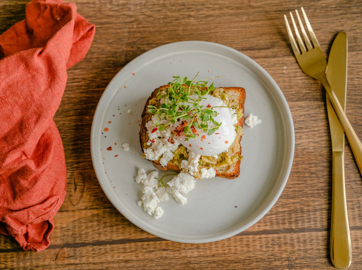 Toast cu avocado zdrobit și ou poșat, presărat cu semințe, pe o farfurie