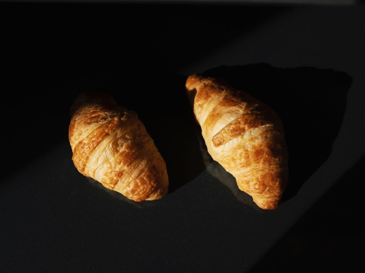 Croissant proaspăt copt, cu textură foietată, pe un platou întunecat