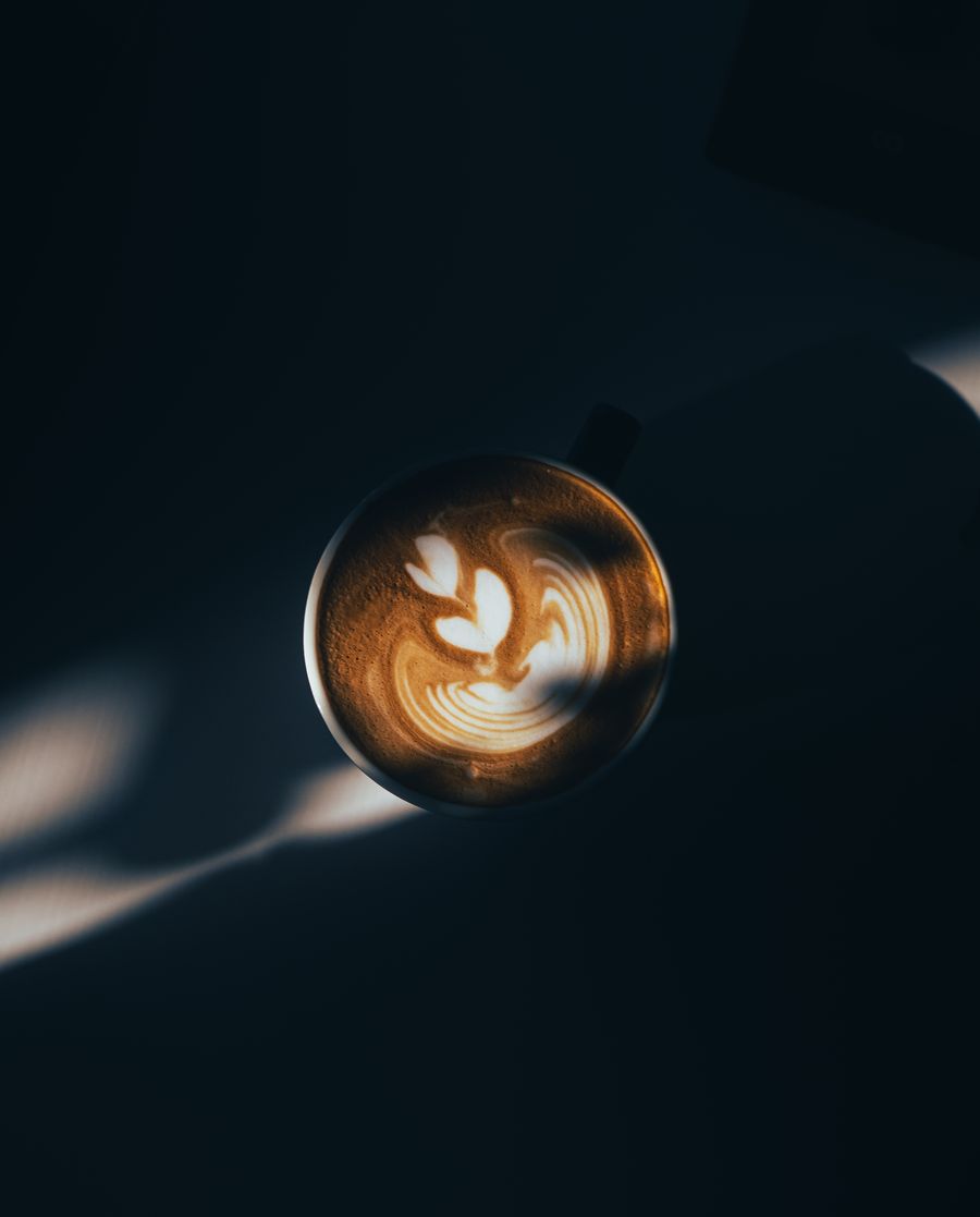 Flat white cu latte art, într-o ceașcă albă pe un blat întunecat