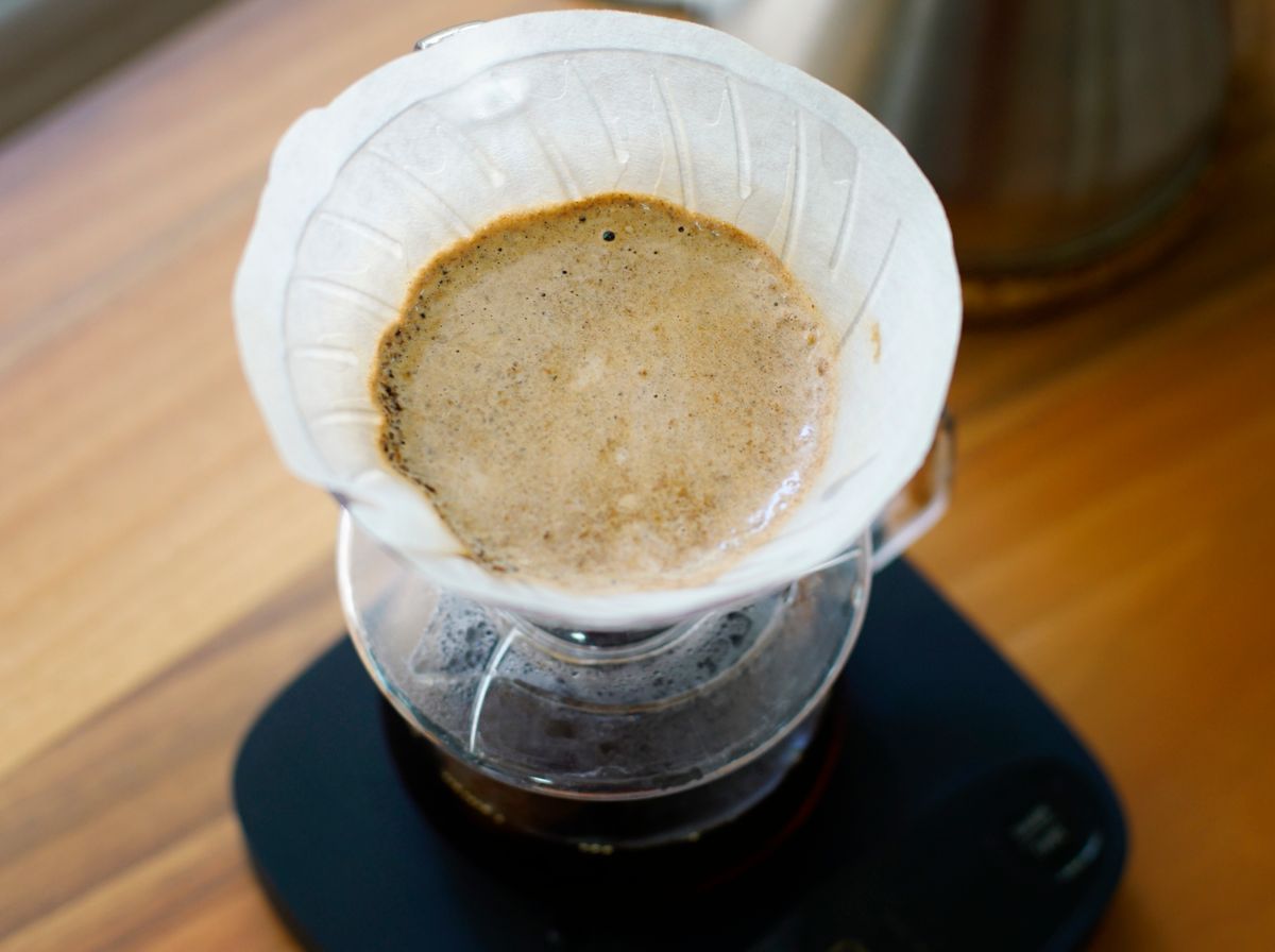 Cafea filtru pregătită manual, văzută de sus, cu ceainic și cântar pe blatul de lemn