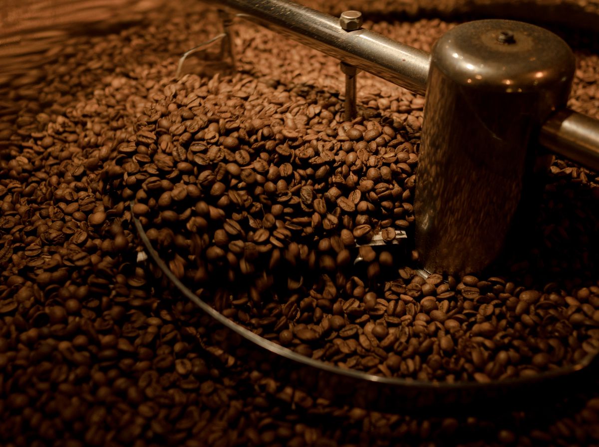 Boabe de cafea proaspăt prăjite, într-un prăjitor industrial, cu textură bogată și tonuri calde